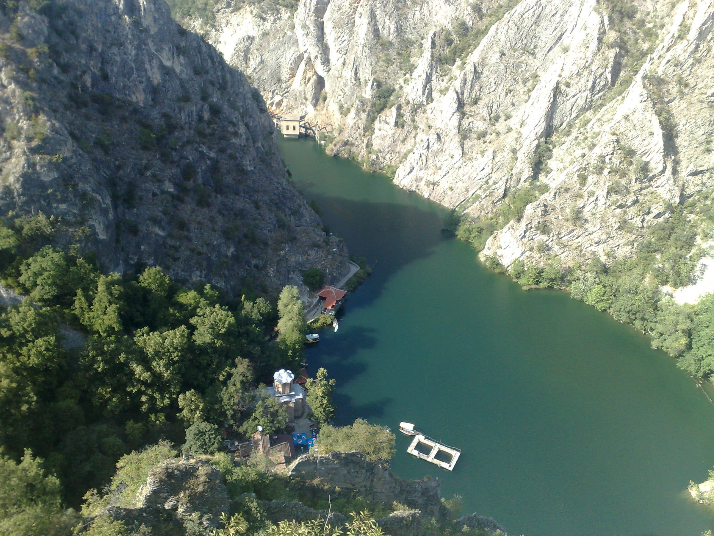 Elevated view down onto a green canyon lake, with a small red-roofed building on the shore beside steep rocky cliffs.