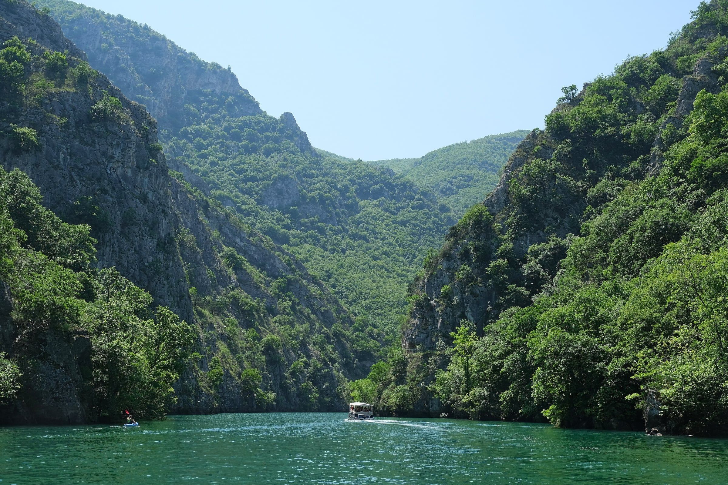Calm green lake running between steep wooded canyon walls, with a small boat on the water.